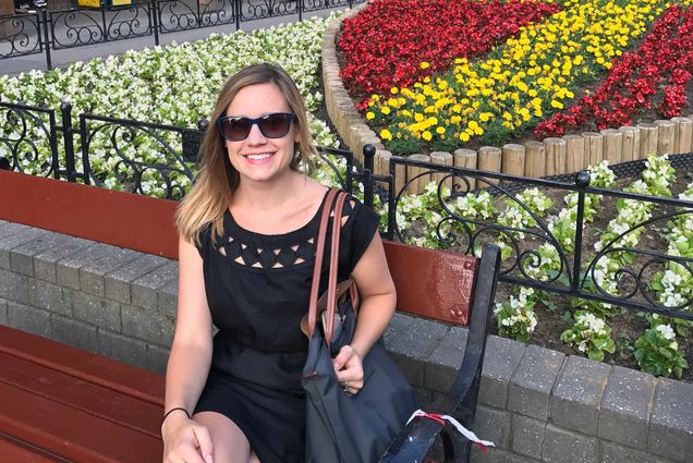 Photo of Carrie O’Connor during one of her many trips abroad. O'Connor was a BU lecturer in French who was killed Monday in an elevator accident. In the photo, she wears sunglasses and smiles on a bunch near a garden of flowers.