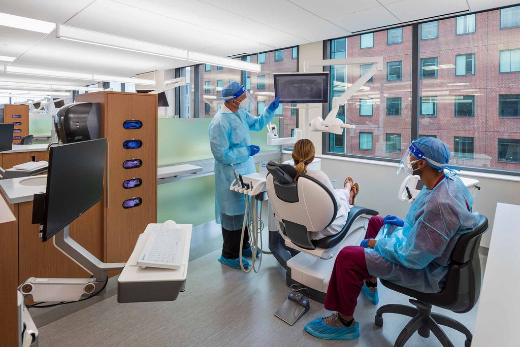 A patient sits in the dentist chair at the Goldman Dental School Dentsply Serona Patient Treatment Center, with two predoctoral students who will treat the patient.