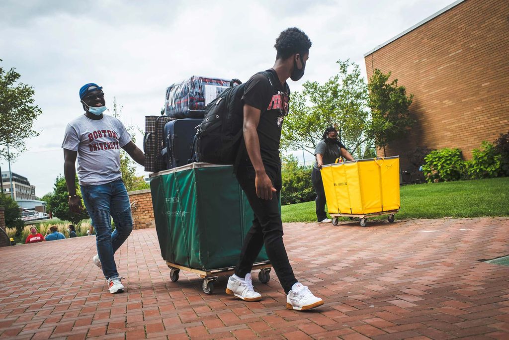 Photo of a student and possibly his father walking with a green moving build filled high with his belongings.
