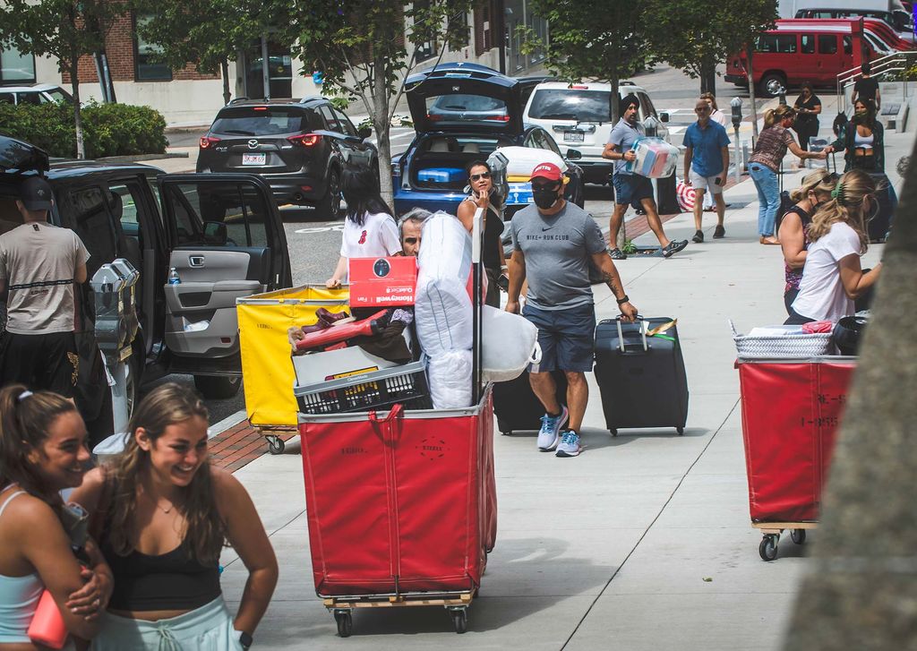 Photo of a busy sidewalk of people during move-in, some push red bins, others push yellow.