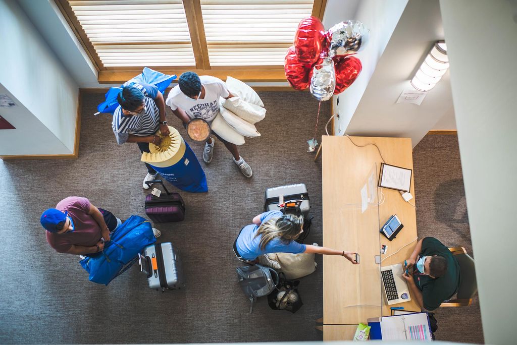 Aerial shot of Resident Assistant, Geo Ferrari checking in students at Stuvi 1 during move-in on Saturday, August 28, 2021. Red and white balloons are seen to the right of the desk and four people stand waiting to be helped.