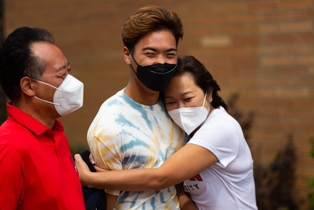 Photo of a student getting hugged by his mom with his dad standing at his right. They all wear facemasks.