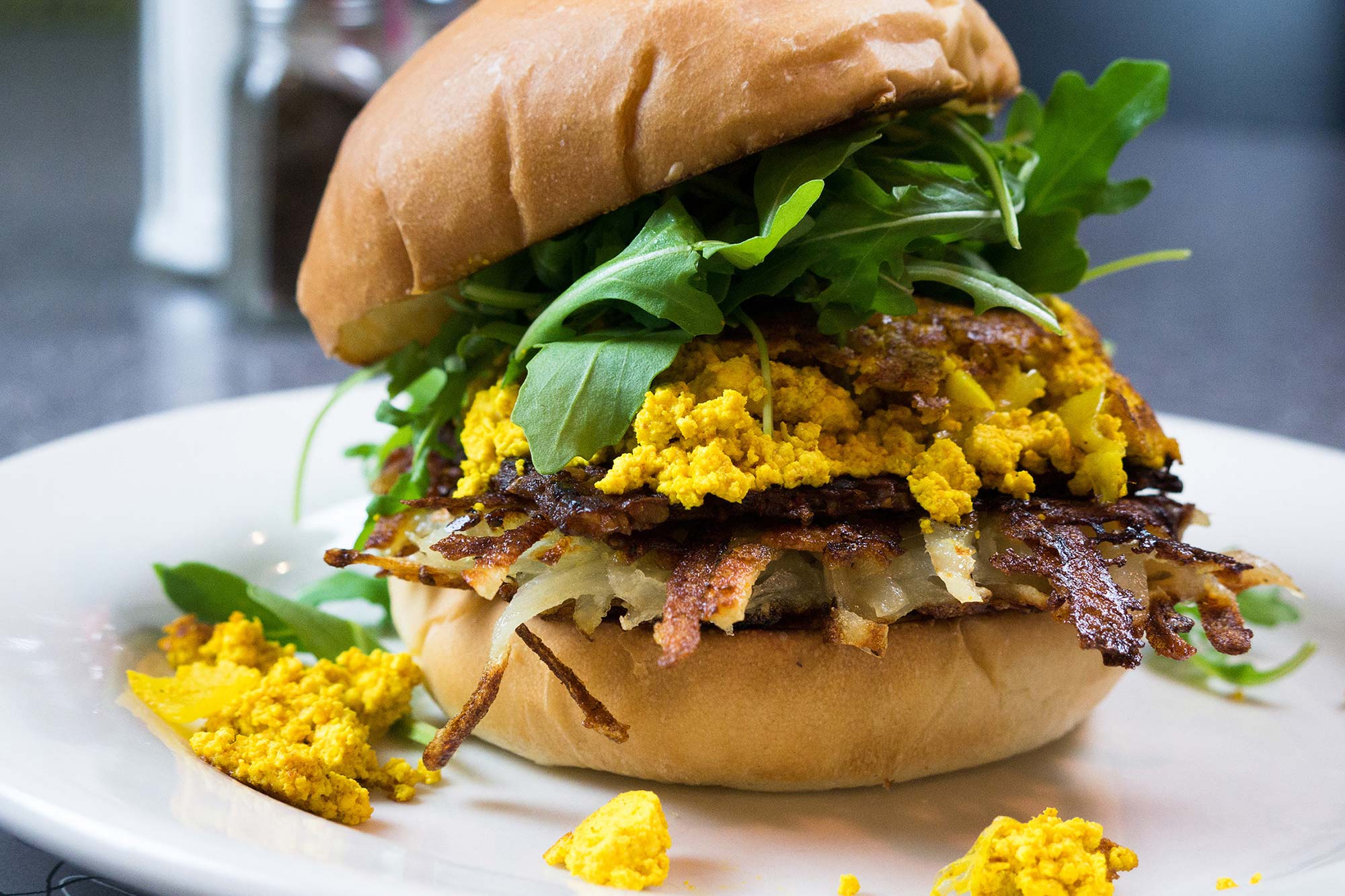 Photo of a Galaxy Burger from Veggie Burger, which has beet lentil mushroom burger with lettuce, tomato, and garlic mayo. The burger filling is bright yellow with arugula on top.