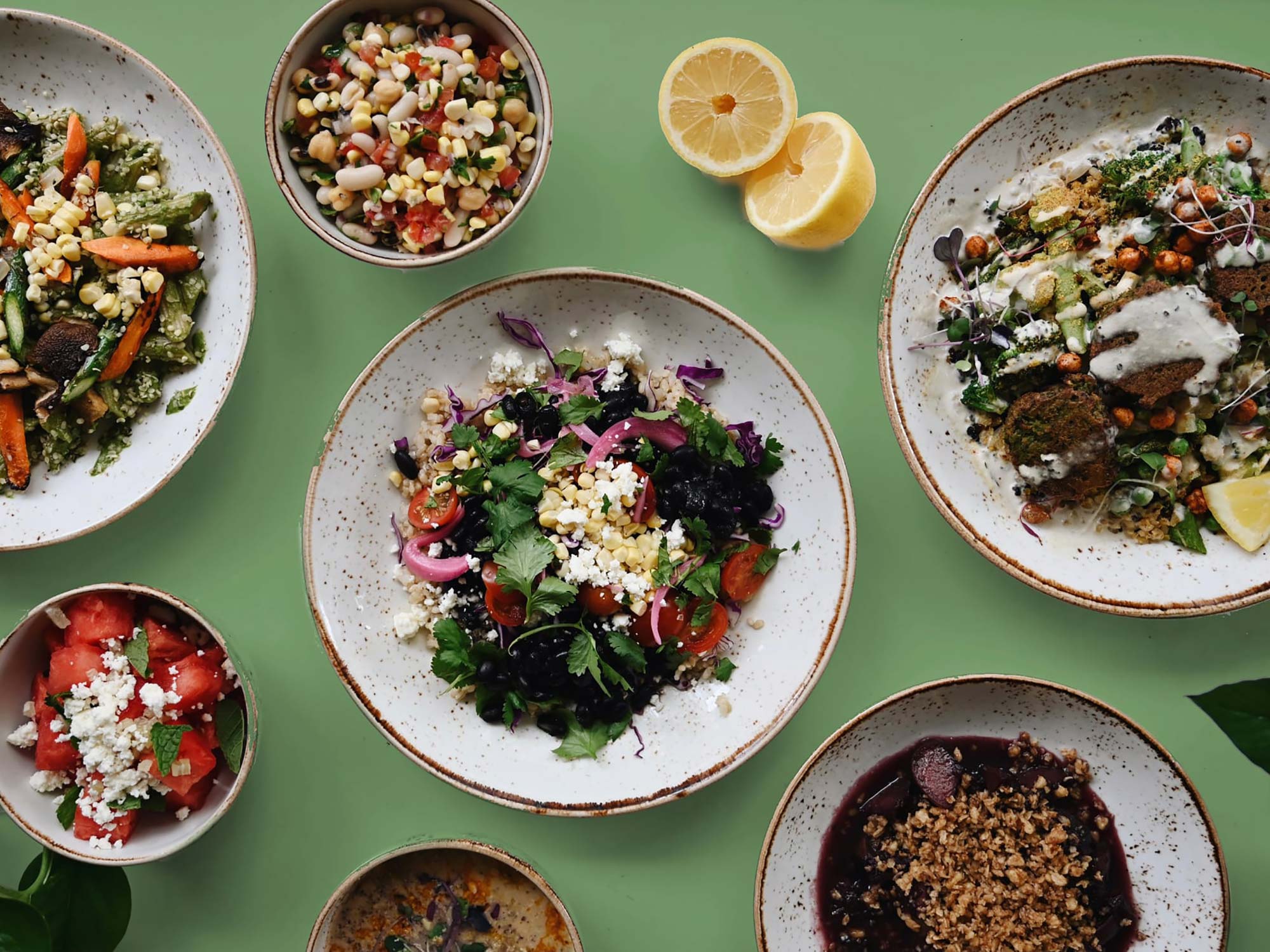 Photo of Life Alive’s spring meal plan. The photo features several rustic-looking bowls filled with greens, vegetables, falafel and other ingredients, topped with either a cheese or sauce. The plates rest on a green surface.