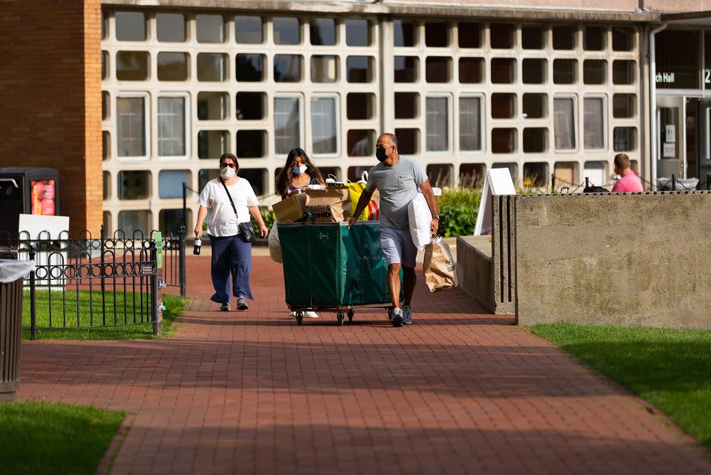 A family wheels a green moving bin down a brick path.