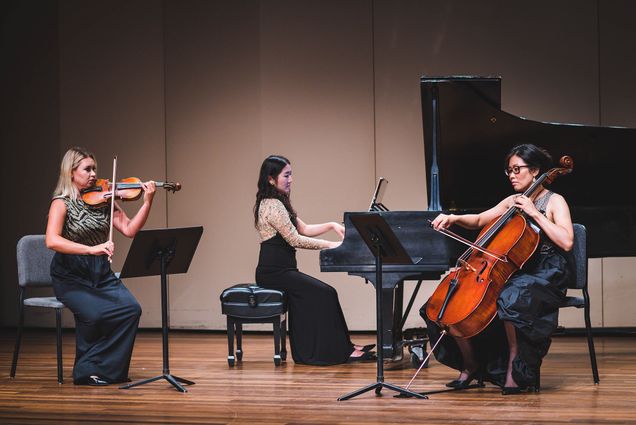 Photo of (Left to right) Egle Jarkova , Han Nah Son, and Cherry Kim recording a memorial concert at the Tsai Performance Center on September 20, 2021. “Remembering Lingzi” will raise money to support the Lu Lingzi Foundation, which honors LIngzi (Questrom’) who was killed in the Boston Marathon Bombings in 2013. The three women wear long black dresses. Jarkova plays the violin, Son sits at the grand piano, and Kim plays the cielo; each woman looks very concentrated.