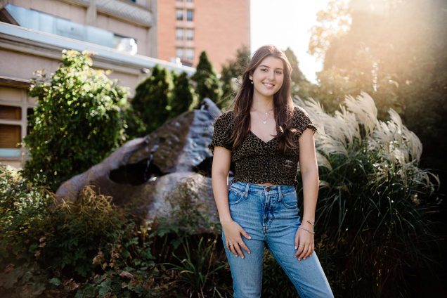 a photo of Student vlogger Anna Malygin posing in front of lush greenery and a well-placed sun-glare highlight on BU's campus