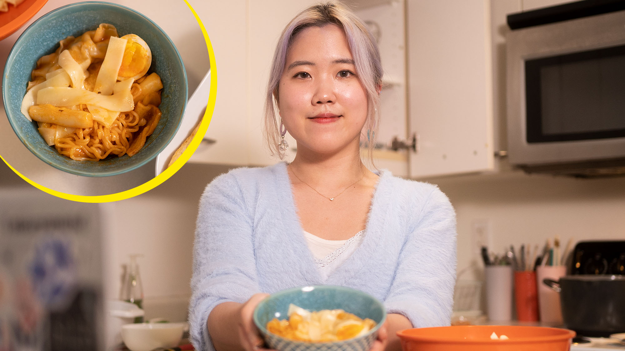 Photo of Sophie Lee (Questrom’22), wearing a light blue sweater and smiling, as she holds a teal bowl of Tteokbokki in front of her. Overlaid on the photo at the top left is a top-down view of the bowl of Tteokbokki, which has noodles, a reddish sauce and a soft-boiled egg.