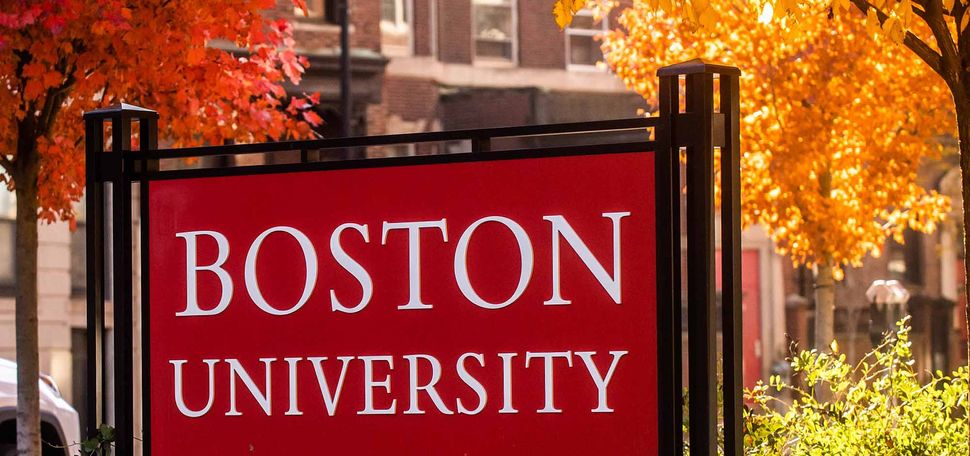 a photo of a red sign that reads "Boston University" surrounded by trees with red and orange fall leaves.