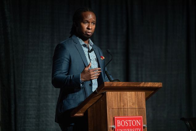 Photo of Dr. Ibram X. Kendi at What the Science Tells Us: Racial Health and Economic Inequities during the Pandemic Symposium presented by The BU Center for Antiracist Research in the Metcalf Hall October 1. He wears a blue suit and a patterned blue button down. He stands at the podium on stage and gestures with his hand as he speaks earnestly.