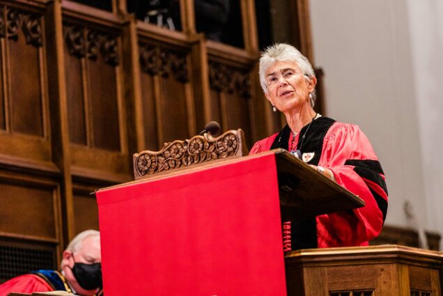 Photo of Yolanda Kakabadse speaking at the 2020 Boston University Baccalaureate Service at Marsh Chapel on October 3, 2021. She wears a red robe and stands at a wooden podium with a red cloth over it.