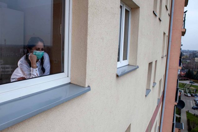 A woman wearing a protective face covering stares sullenly out of her window.