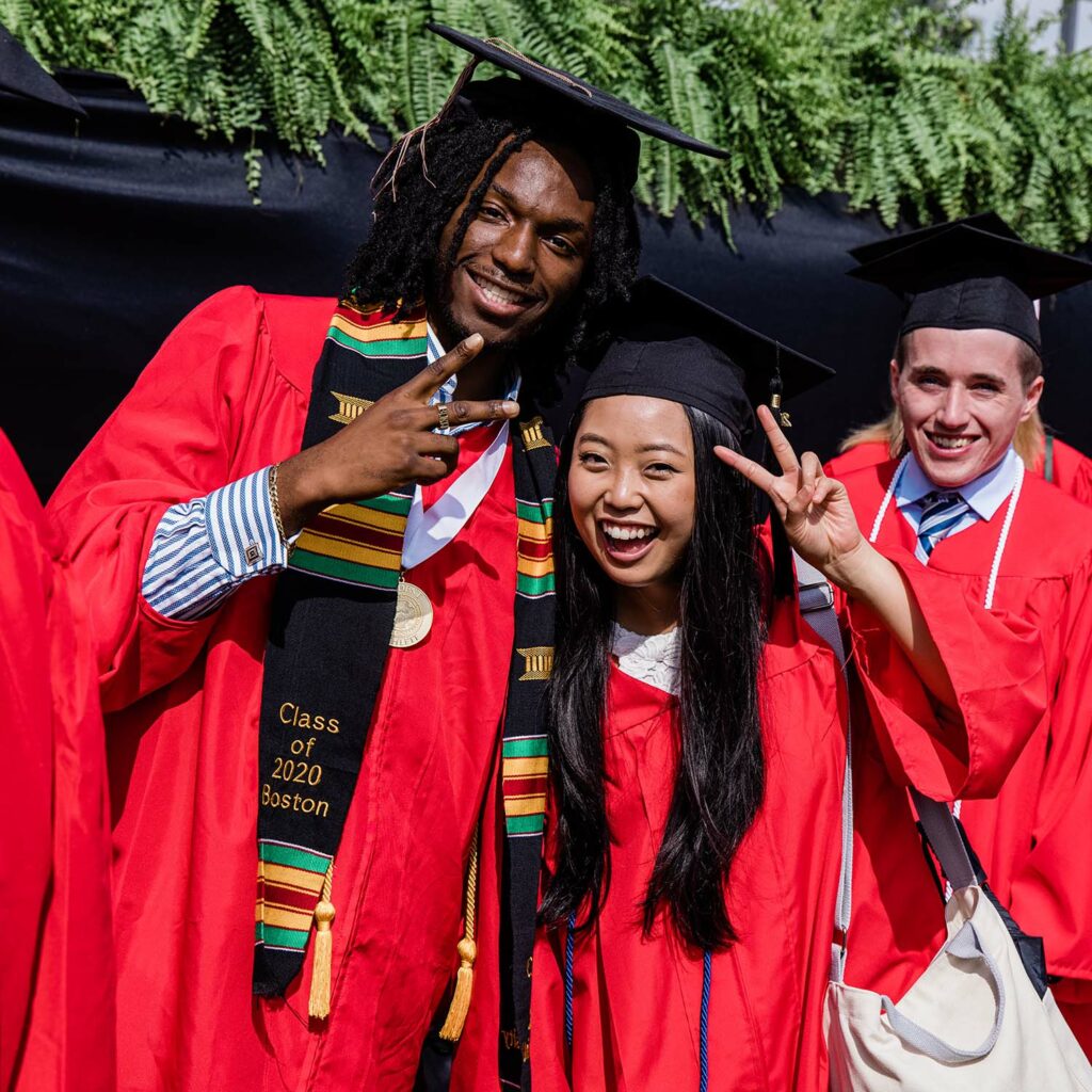 Two students pose for a photo smiling and flashing peace signs for the camera while celebrating on Nickerson Field following BU's Class of 2020 Commencement.