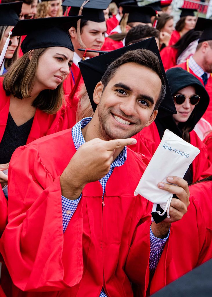 A BU Class of 2020 graduate poses for a photo pointing at the rain poncho package given to graduates on the field.