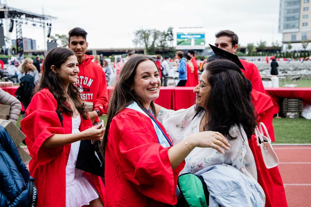 A student smiles as she hugs a family member following Boston University's 147th Commencement ceremony on Nickerson Field.