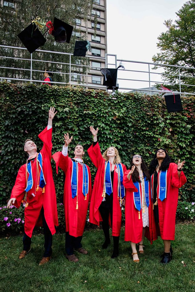 Five Boston University Class of 2020 graduates wearing red robes and blue stoles throw their graduation caps in the air