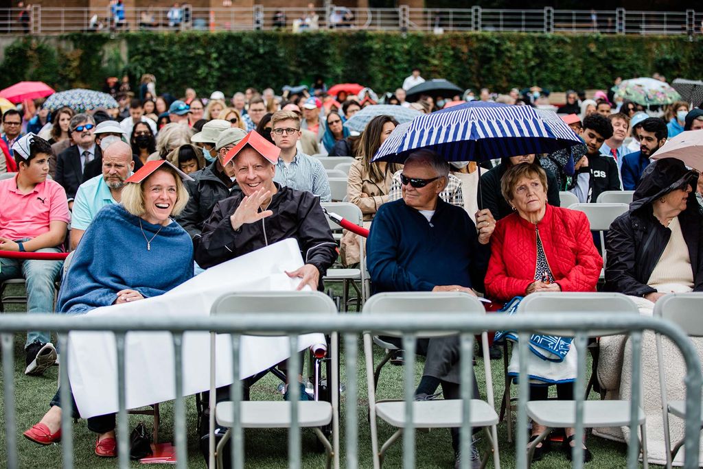 Spectators hold umbrellas, wear hoods, and put open books on their heads to protect them from the rain at Boston University's Commencement on Nickerson Field.