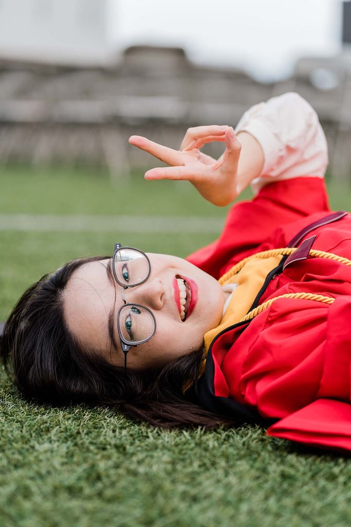 A BU Class of 2020 graduate poses for a photo lying on Nickerson Field and flashing a peace sign.