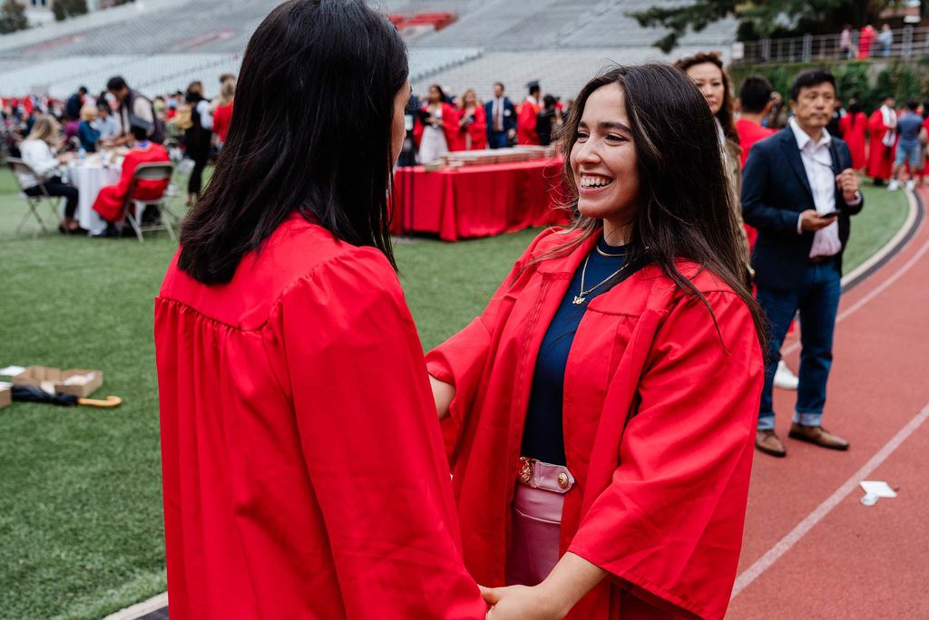 Smiling students talk to each other on Nickerson Field following graduation.