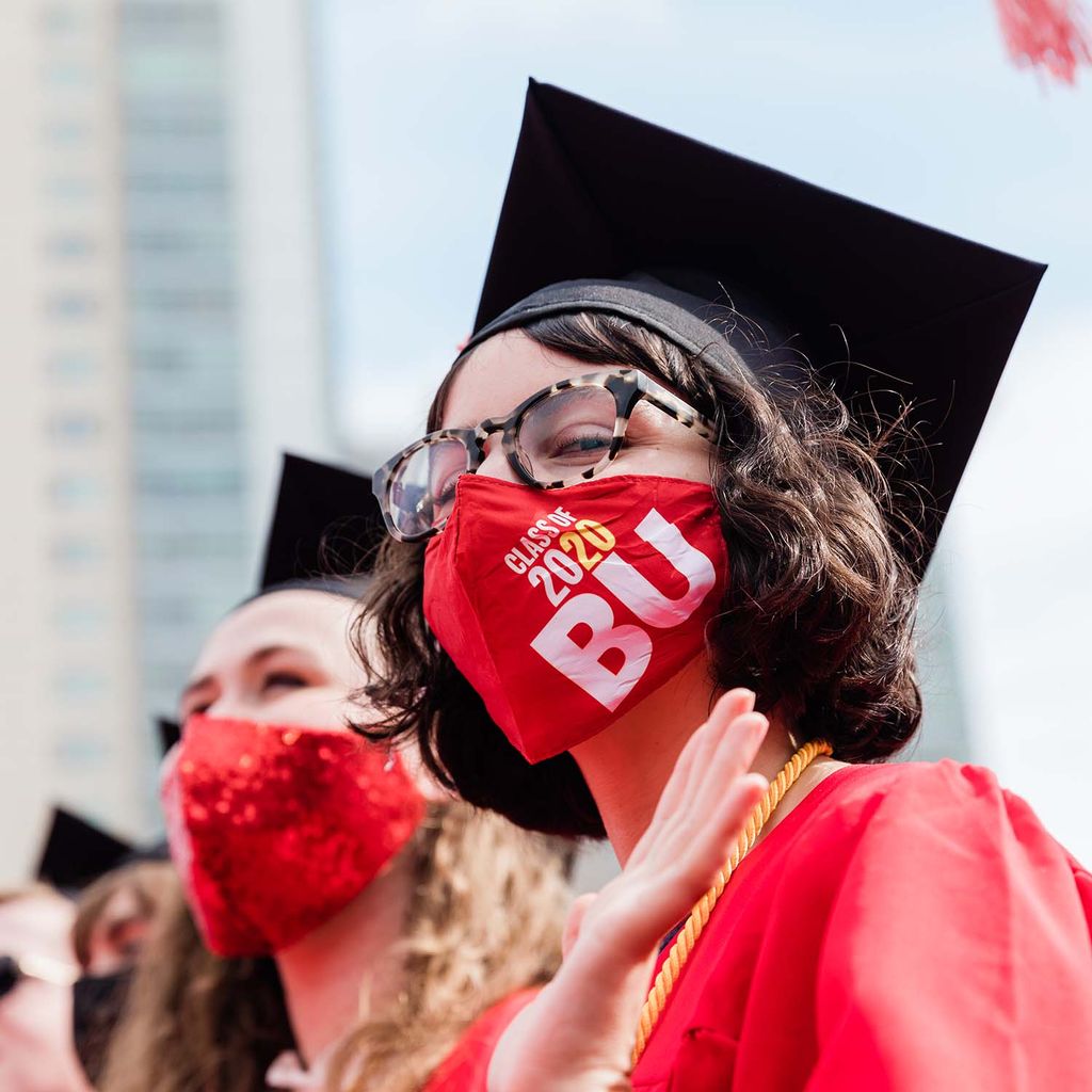 A graduating student wearing a BU Class of 2020 face covering peers down at the camera.
