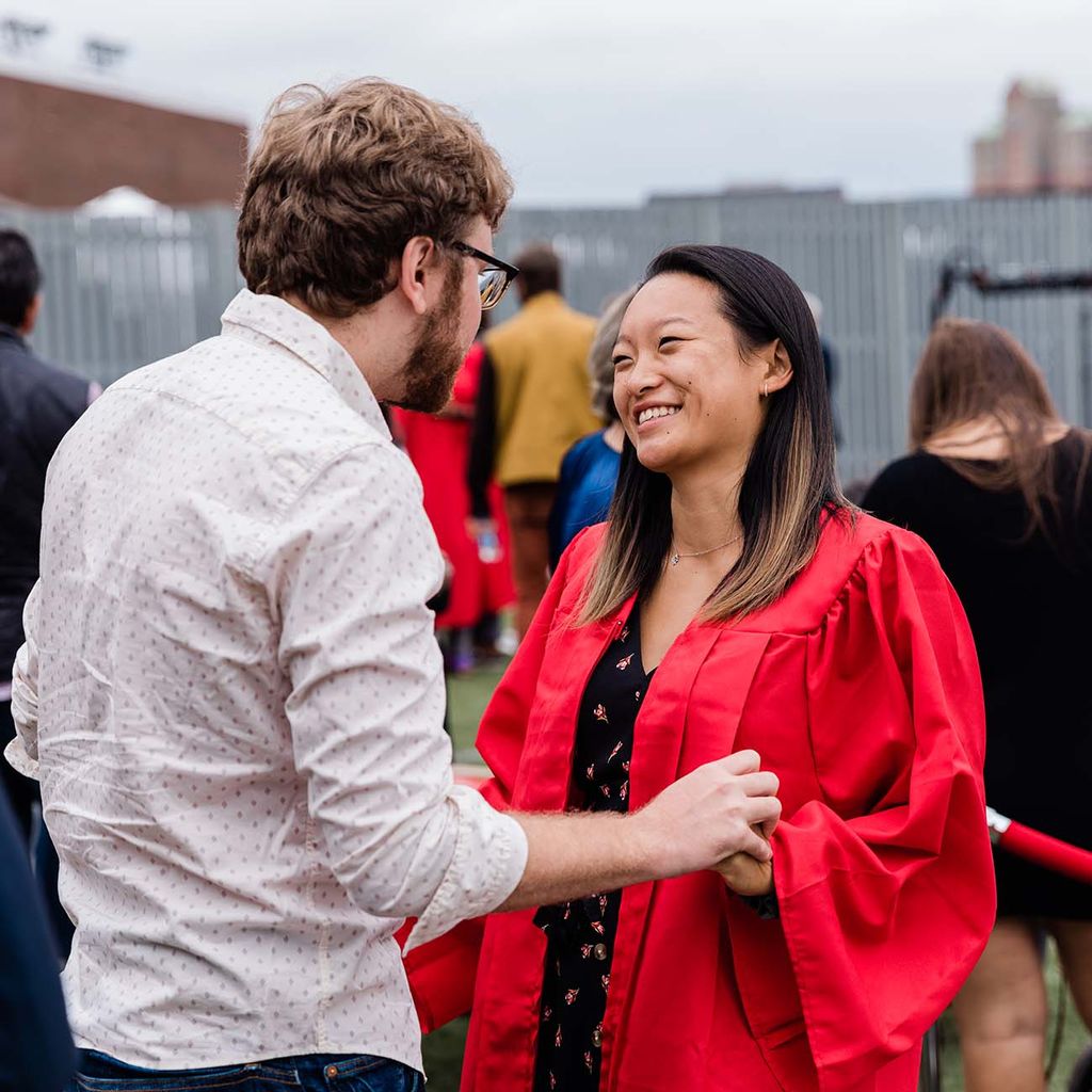 A Class of 2020 graduate smiles and talks to a friend or family member following graduation.