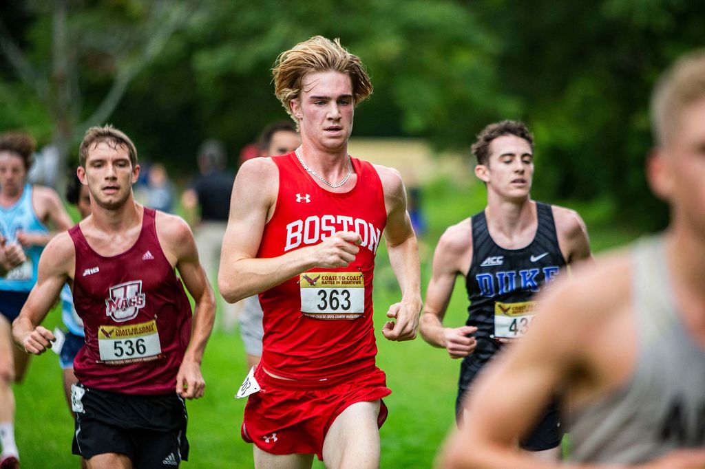 Photo of Matthew Mason (Questrom’24), with a number 363 bib hanging on his red running jersey, mid-stride during a race. His blonde hair bobs as he runs, and he and the other runners around him sweat.