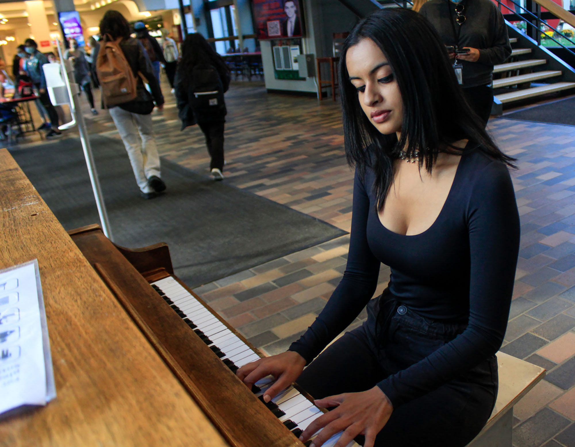 Photo of Musician Radha Rai (QST '21) playing piano at the GSU after undergoing a series of interviews regarding her encounter with famous singer John Legand the day prior. She wears a black top and pants, and looks contently at the piano as she plays.
