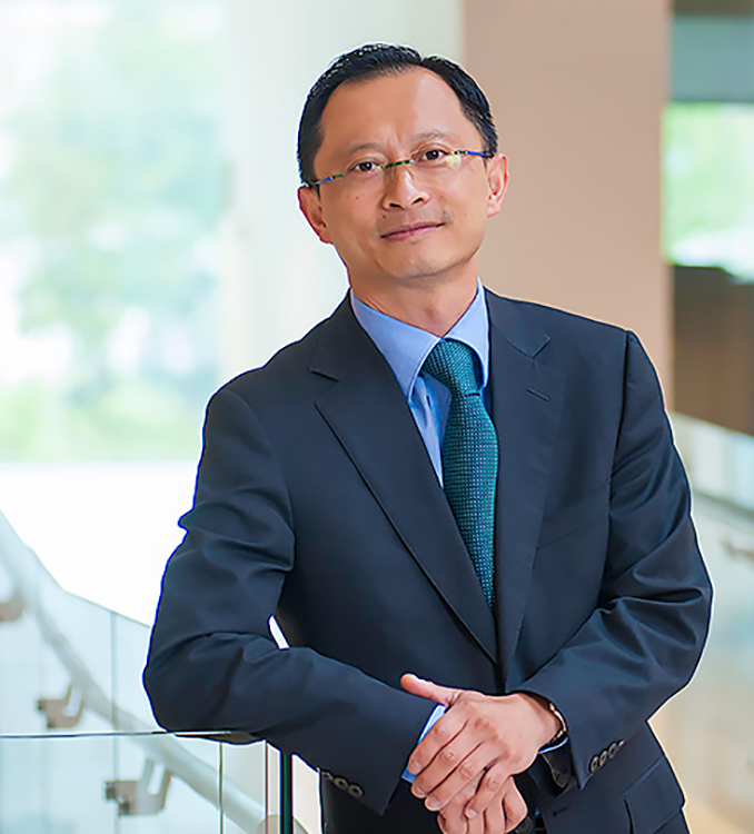 Portrait of Incoming LAW Professor Robert Tsai in a suit learning on a railing and smiling.