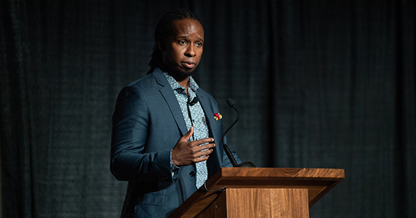 Photo of Dr. Ibram X. Kendi at What the Science Tells Us: Racial Health and Economic Inequities during the Pandemic Symposium presented by The BU Center for Antiracist Research in the Metcalf Hall October 1. He wears a blue suit and a patterned blue button down. He stands at the podium on stage and gestures with his hand as he speaks earnestly.