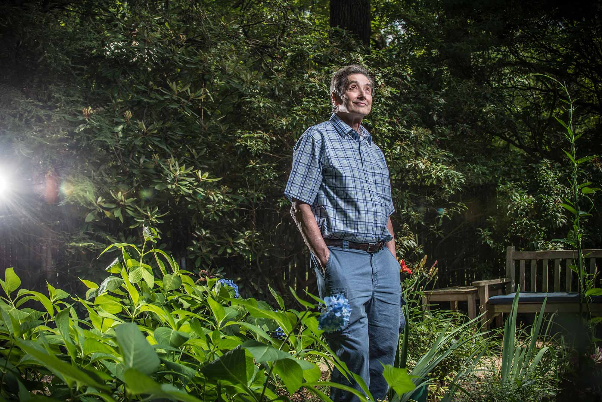 Neuroscientist Stephen Grossberg standing in his yard looking up at the sky with a light shining behind him.