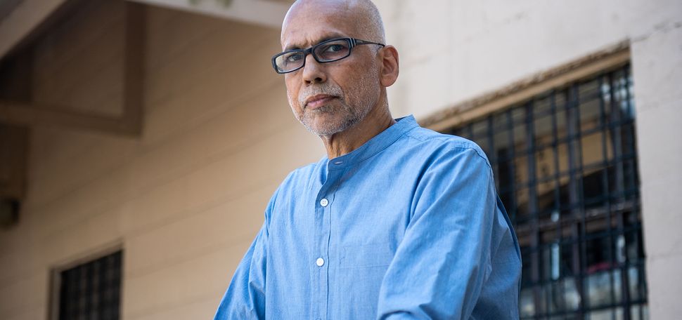 photo of André de Quadros, choir director and teacher of music in the BU prison education program, looking at the camera with a stoic expression. He wears black, rectangular glasses and a light blue collared shirt.