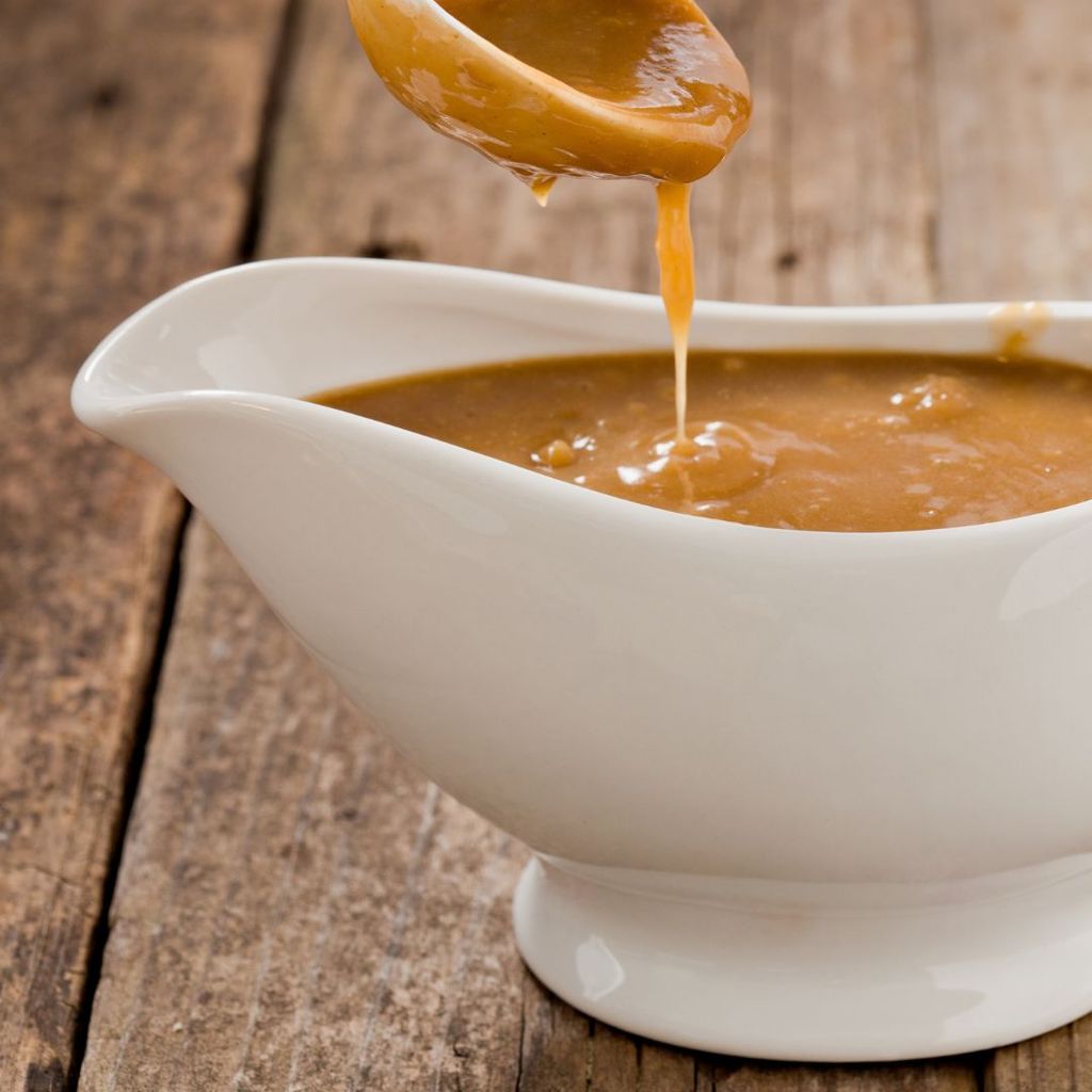 An up-close shot of a small white ladel pouring brown gravy into a white ceramic gravy bowl.