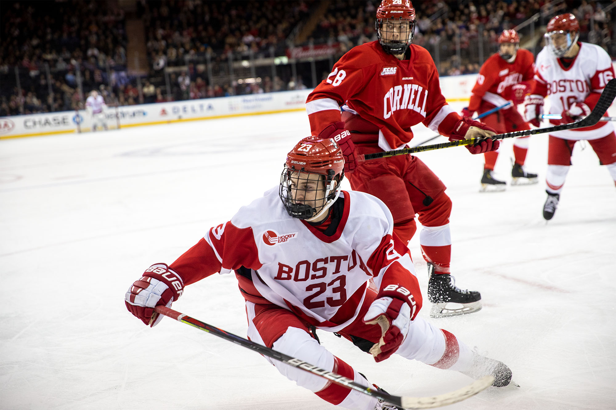 closeup photo of Dom Fensore during the Red Hot Hockey games 2 years ago. He wears a white jersey and skates with puck away from a Cornell athlete donned in all red.