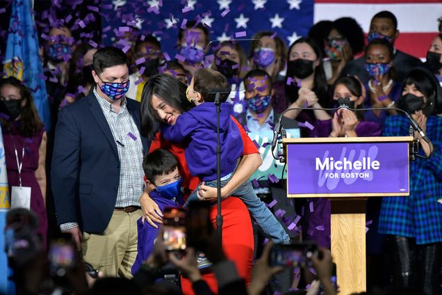 Michelle Wu stands on stage next to a podium reading "Michelle For Boston", with her family after being elected Mayor of Boston