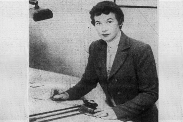 Photo of Anne Everest Wojtkowski (1935-2014), the first woman to graduate from the Boston University College of Industrial Technology. The photo is black and white and pictures Wojtkowski writing at a desk with a lamp. She has short dark hair.