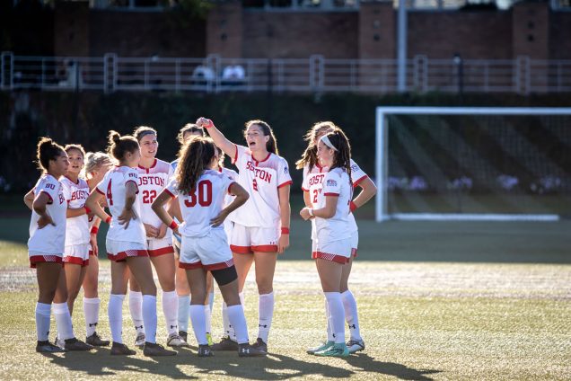 Photo of Ashley Buck (Sargent’22), number 2, pointing, surrounded by the rest of the BU women’s soccer senior class on their home turf at Nickerson Field as first-year players in 2018. They wear white and red jerseys.