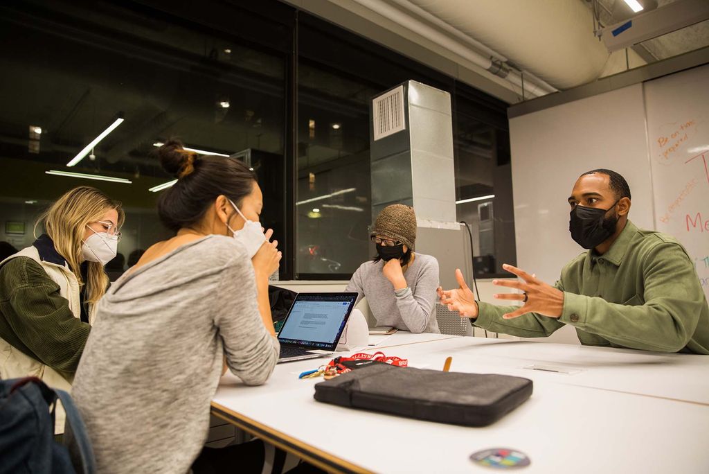 Photo of Jonathan Allen, right, chatting with, clockwise from left, Kati Nalbandien (MET’22), Sohyoung Park (CFA’23) and  Elle Zeng (MET’22) about their self sustaining ecosystem project during a a speed mentoring session at the BUild Lab Monday, October 25, 2021. The group wears face masks and sits around a white table with their laptop open.