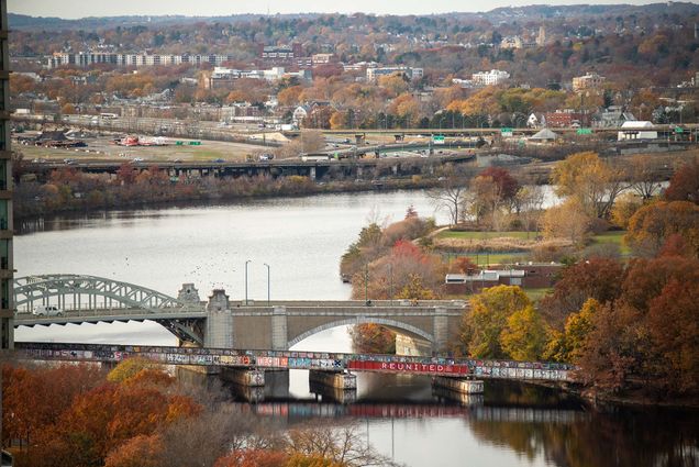 Photo of a view of the BU Bridge from the fourteenth floor of the Center for Computing & Data Sciences November 17. The water of the Charles River is pale, gray-blue, and orange and yellow-leafed trees are seen in the foreground.