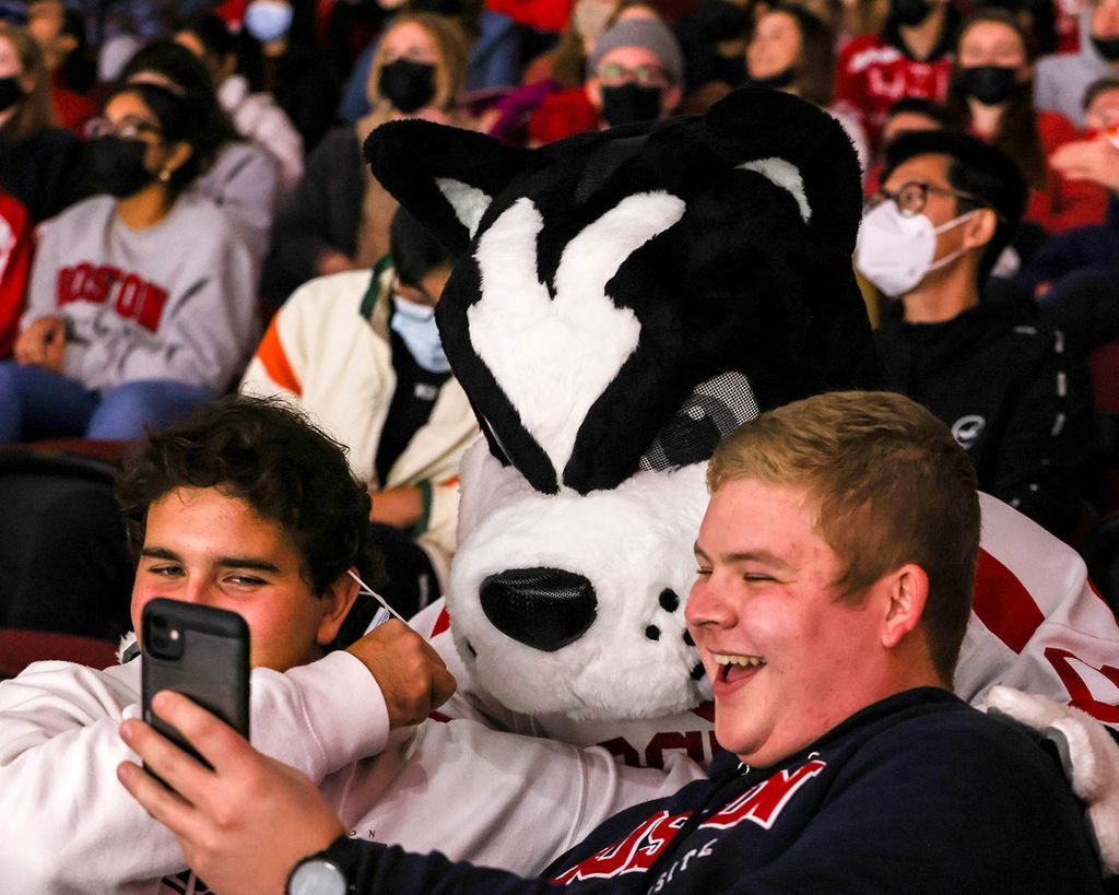 Photo of students taking a selfie with Rhett during a hockey game. The crowd wears BU Swag and boys smile as they pose for the photo.