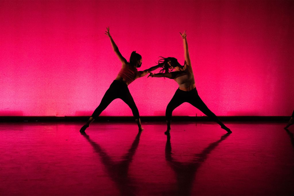 Two dancers pose against a red/orange background on a stage