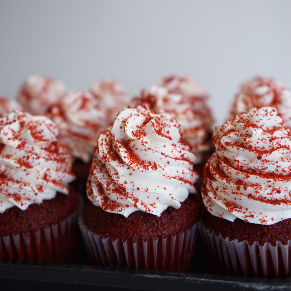 Photo of a row of red velvet cupcakes from Lyndell's bakery. A tall swirl of white frosting is dusted with red springles.