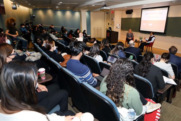 Photo taken from behind students in an auditorium attending the SHA Dean’s Distinguished Lecture Series, with Katie Potter, president and chief executive officer of Five Star Senior Living, and Arun Upneja, dean of SHA, who are sitting at the front of the room on stage.