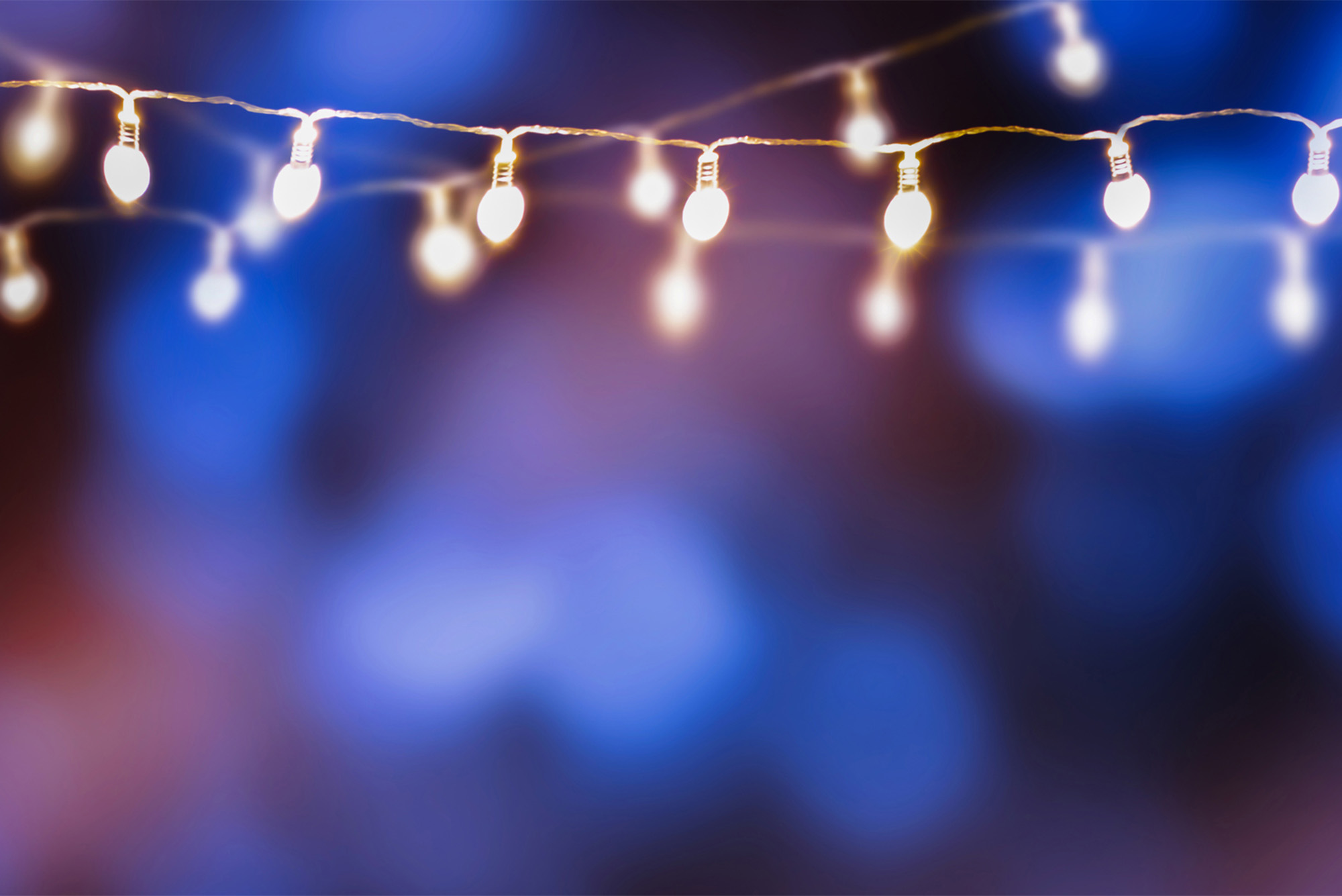 a string of holiday lights in front of a blurred blue background