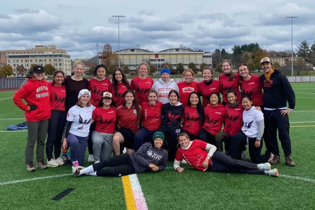 Photo of the women's ultimate frisbee team at Regionals. The group of roughly two dozen women wear red BU jerseys and pose for a photo on the turf field.