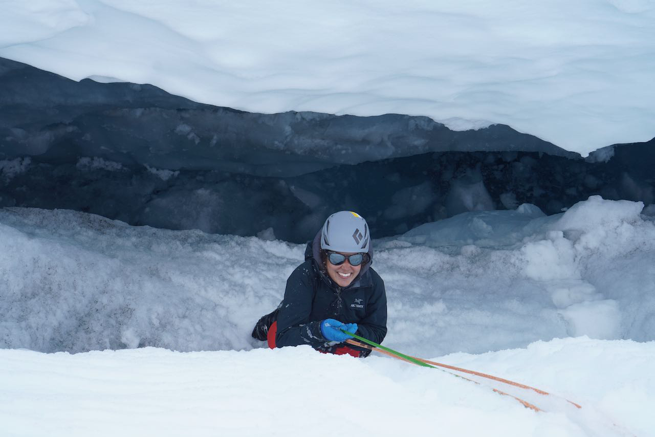 photo of BU student Anne Randall being lowered into a crevasse, held up by an anchor system built into the snow. A haul team then hoisted her up, one of the skills taught to students during the safety training weeks at JIRP.