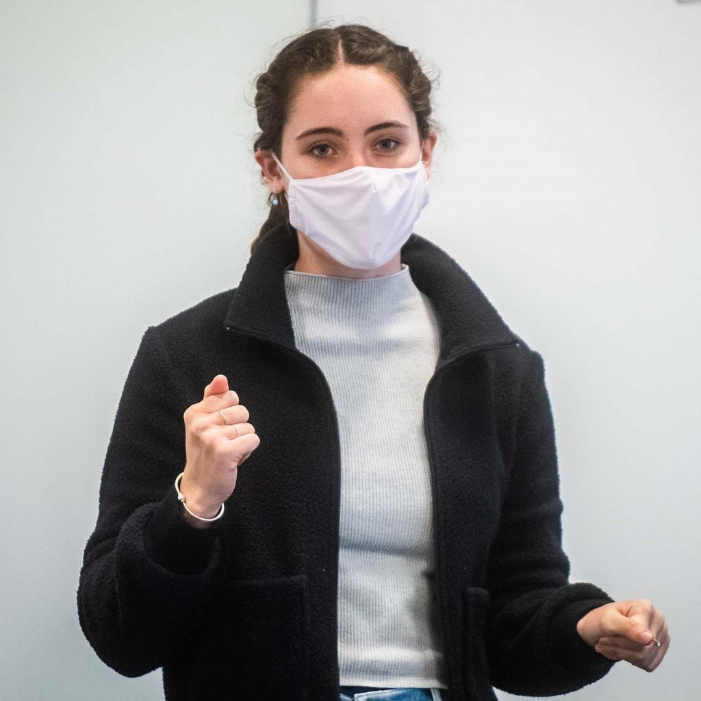 Photo of Isabel Janeff (Sargent’23), wearing a white face mask, black jacket, and french braids.