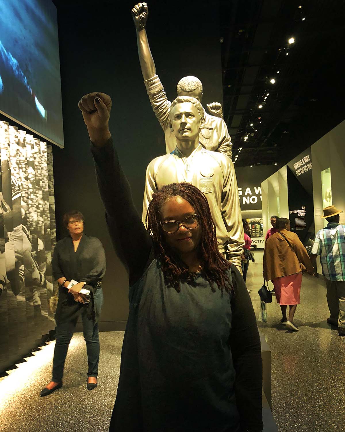 Photo Douglas in a black blouse standing with her right first raised in front of a statue.