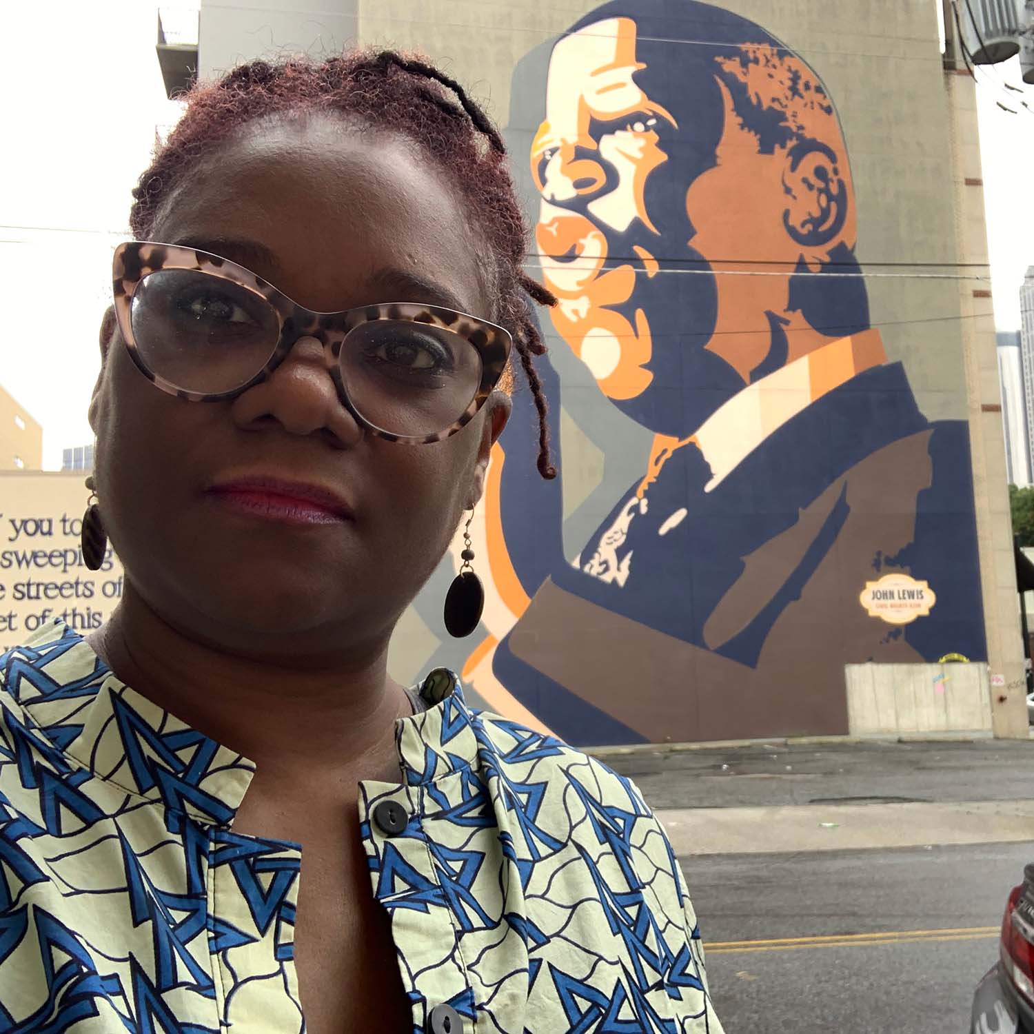 Selfie of Douglas with a mural of John Lewis painted on an underpass in the background.