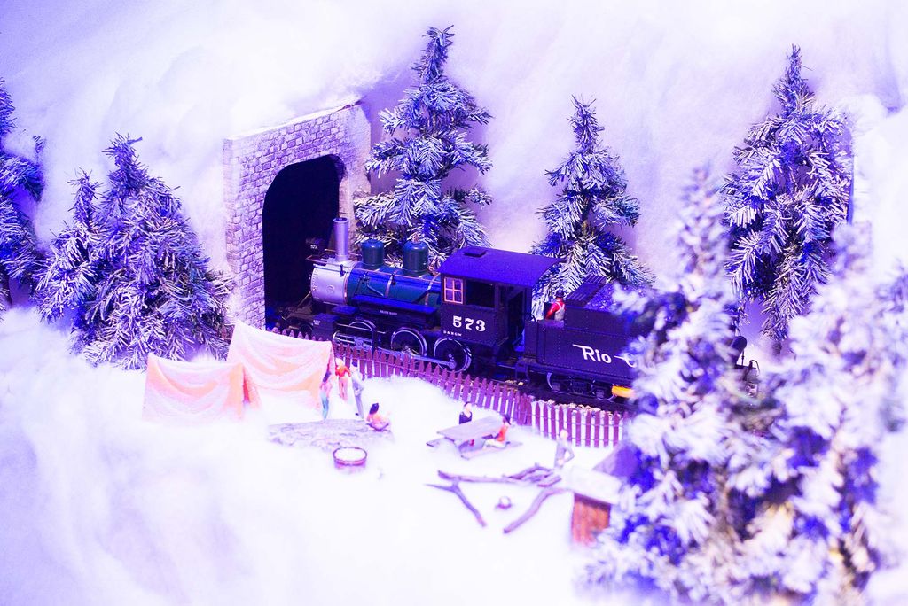 Photo of a miniature train about to enter a tunnel at The Museum of Science’s annual holiday exhibit. A snowy landscape is seen, with snow-covered trees and figurines of people at a picnic.