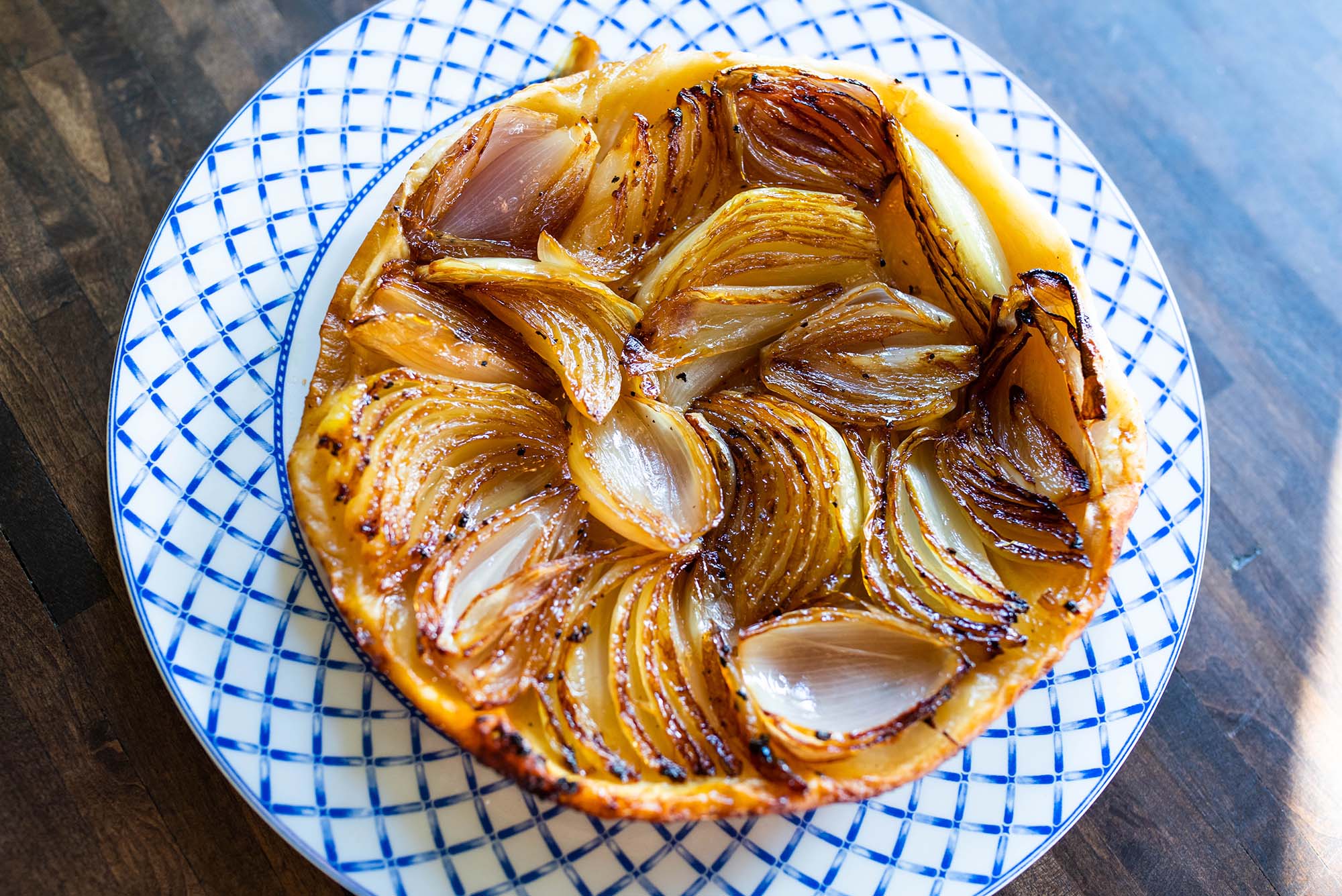 photo of an onion tarte tatin. The onions are nice and carmelized; the tarte rests on a white plate with a blue border.